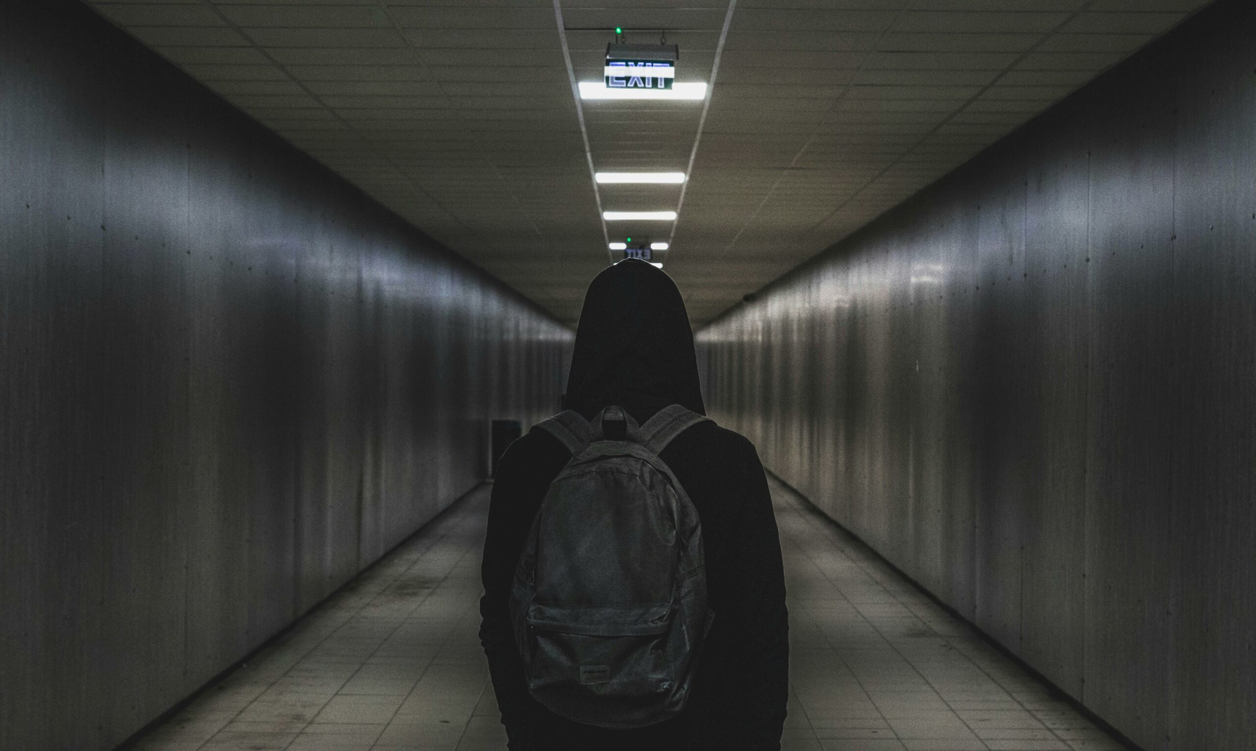 A person with a backpack walks through a dimly lit tunnel, conveying mystery and solitude.